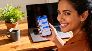 Emprendedora colombiana sonriendo mientras revisa mensajes de clientes en su teléfono, en su espacio de trabajo y conectando con su audiencia